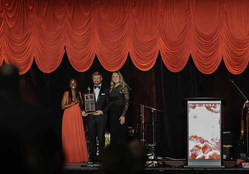 Three people standing on stage holding an award up while audience gives a standing ovation.
